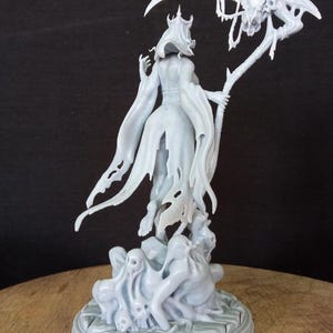 May include: A white, skeletal figure with a crown and tattered robe holds a scythe with a skull at the end. The figure stands on a base with smaller skeletal figures.