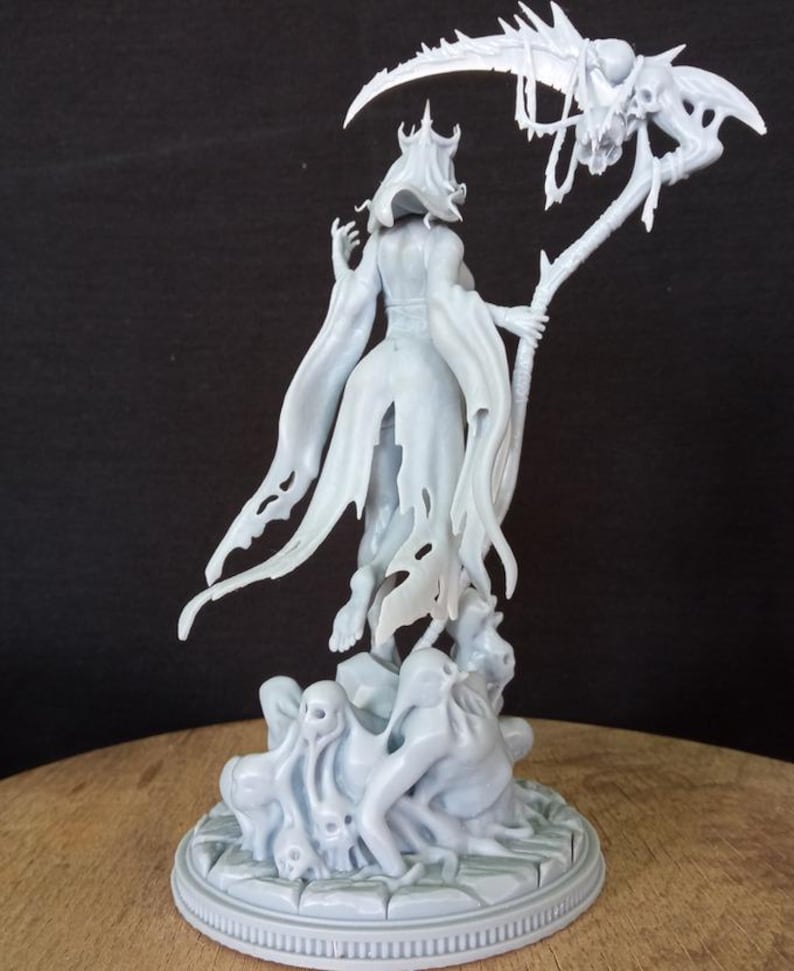 May include: A white, skeletal figure with a crown and tattered robe holds a scythe with a skull at the end. The figure stands on a base with smaller skeletal figures.
