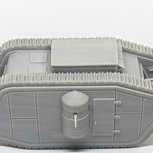 Puede incluir: Un modelo de pl&aacute;stico gris de un tanque de la Primera Guerra Mundial. El tanque tiene una torreta grande y rectangular en la parte superior y una torreta cil&iacute;ndrica m&aacute;s peque&ntilde;a en el lateral. El tanque tiene orugas en ambos lados y una escotilla grande y rectangular en la parte posterior.