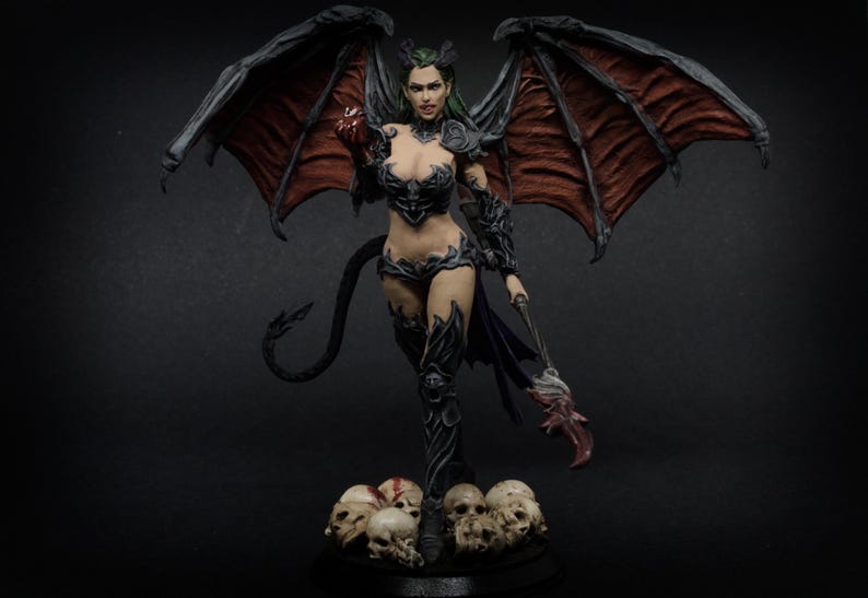 May include: A detailed figurine of a female demon with large, dark wings and a long tail. She wears black armor and stands on a base of skulls. The figure holds a glowing orb and a staff with a claw-like end. The wings are a deep red.