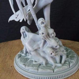 May include: A gray 3D printed figurine of a winged figure standing on a base with multiple smaller figures. The base is textured and has a circular design.