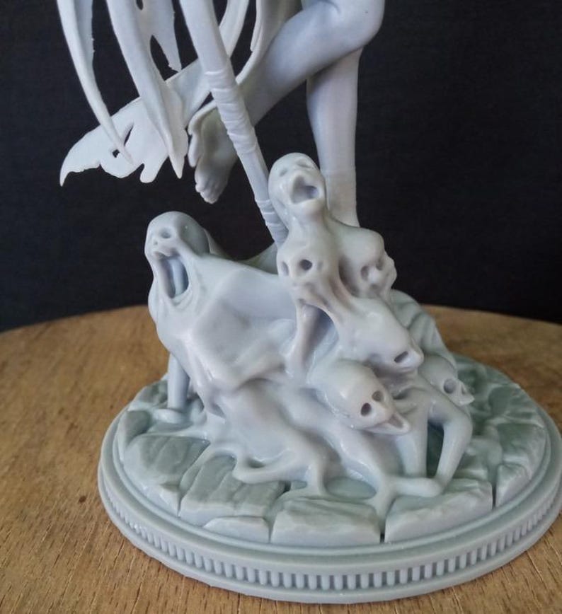 May include: A gray 3D printed figurine of a winged figure standing on a base with multiple smaller figures. The base is textured and has a circular design.