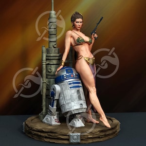 Op de afbeelding: Gedetailleerd beeldje met een vrouw in een gouden en groene bikini die een blaster vasthoudt, leunend tegen een blauw-witte droid. Achter hen staat een hoge, cilindrische structuur. De basis is donkerbruin.