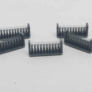 Puede incluir: Cinco secciones de v&iacute;a de tren modelo de pl&aacute;stico gris, cada una con una serie de peque&ntilde;as aberturas rectangulares. Las secciones est&aacute;n dispuestas en forma escalonada sobre una superficie blanca.