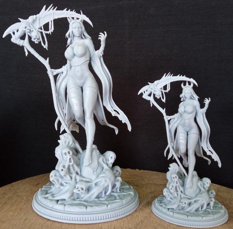 May include: Two white painted resin figurines of women with long hair, wearing robes and holding scythes. The figurines are standing on bases with skulls and bones.