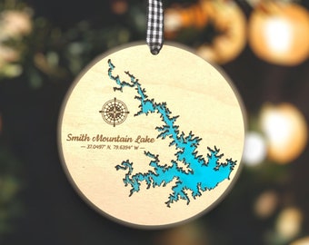 May include: A wooden Christmas ornament featuring a blue outline of Smith Mountain Lake, North Carolina. The ornament includes the coordinates 37.0497° N, 79.6394° W.