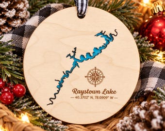 May include: A round wooden ornament featuring a laser-cut map of Raystown Lake with a bright blue inlay, a compass rose, and the text Raystown Lake 40.3702 N, 78.0909 W, suspended by a black and white gingham ribbon.
