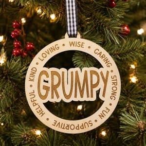 May include: A circular wooden ornament featuring the word GRUMPY in large letters at the center, surrounded by the words WISE, CARING, STRONG, FUN, SUPPORTIVE, HELPFUL, KIND, and LOVING. The ornament hangs from a black and white gingham ribbon.