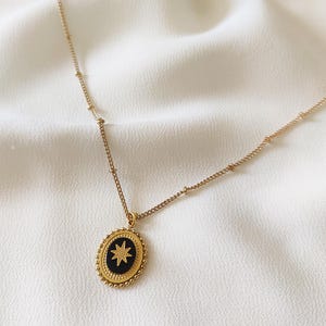 May include: A gold chain necklace with a gold oval pendant featuring a black starburst design.