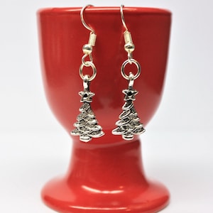 May include: A pair of silver dangle earrings featuring a Christmas tree design. The trees have a star on top and are made of a textured metal.