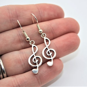 May include: A pair of silver earrings featuring a treble clef design. The earrings are dangle style with a silver hook.