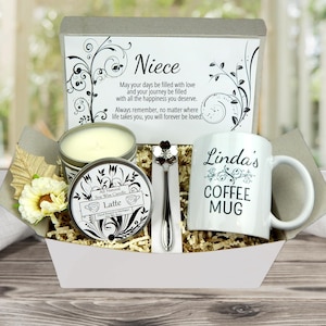 May include: A gift basket containing a white coffee mug with "Linda's COFFEE MUG" printed on it, a soy wax candle, a decorative spoon, and a card with the word "Niece" and a message. The basket includes decorative flowers and filler.