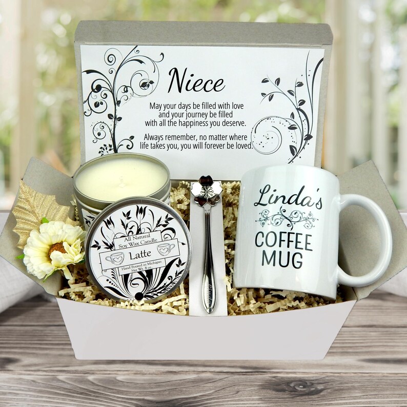 May include: A gift basket containing a white coffee mug with "Linda's COFFEE MUG" printed on it, a soy wax candle, a decorative spoon, and a card with the word "Niece" and a message. The basket includes decorative flowers and filler.