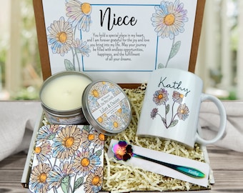 May include: A gift box containing a white mug with a daisy design and the name "Kathy", a candle, a coaster, and a spoon. The box also includes a card with the word "Niece" and a message about joy and love.