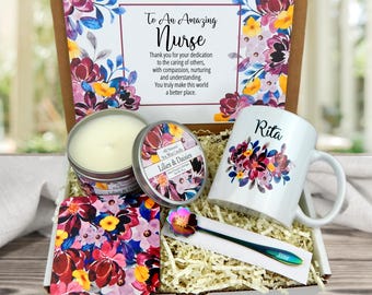 May include: A gift box for a nurse containing a white ceramic mug with the name Rita and floral art, a soy wax candle labeled Lilies & Daisies, a square floral coaster, and a metal spoon with a flower handle, plus a card with a floral border.