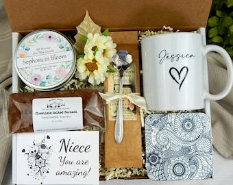 May include: A gift box filled with items for a niece. The box contains a white mug with the name "Jessica" and a heart, a small bag of coffee, a small bag of biscotti, a soy wax candle, a small spoon, and a decorative coaster.