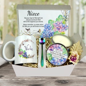 May include: A gift basket containing a white mug with a floral design and the name "Vickie", a decorative spoon, a candle, and a card with the word "Niece" and a poem. The basket includes decorative paper and a floral accent.