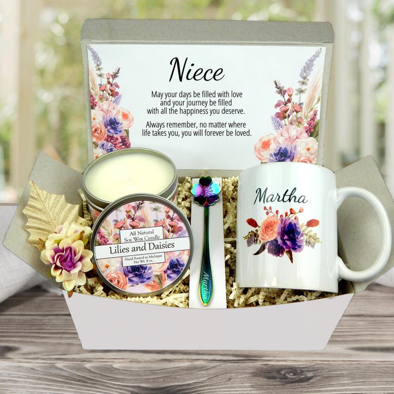 May include: A gift basket containing a mug with the name "Martha", a candle, a decorative spoon, and a card with the word "Niece" and a message. The mug and card are decorated with floral designs. The candle is labeled "Lilies and Daisies".