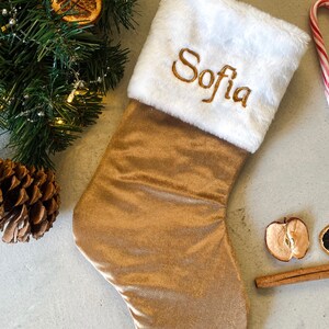 May include: A gold velvet Christmas stocking with a white faux fur cuff. The stocking is personalised with the name "Sofia" embroidered in gold thread.