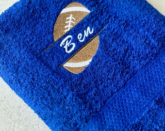 May include: A blue towel with a brown football embroidered on it. The football has a white stitched design and the name "Ben" is embroidered on a white banner.