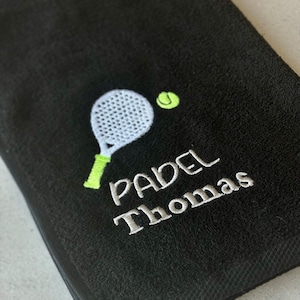 Puede incluir: Toalla negra con un paddle y una pelota bordados en blanco y verde, y el texto "PADEL Thomas" en blanco.