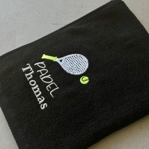 Puede incluir: Toalla negra con bordado blanco de una raqueta de p&aacute;del y una pelota, y el texto "PADEL Thomas".
