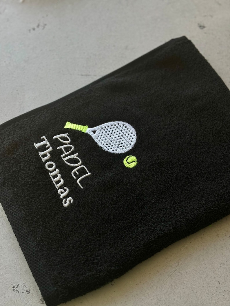 Puede incluir: Toalla negra con bordado blanco de una raqueta de p&aacute;del y una pelota, y el texto "PADEL Thomas".