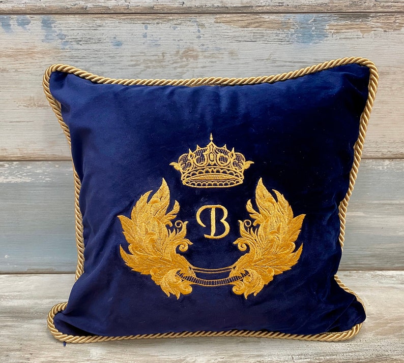 May include: A navy blue velvet pillow with a gold embroidered crown, wings, and the letter "B".