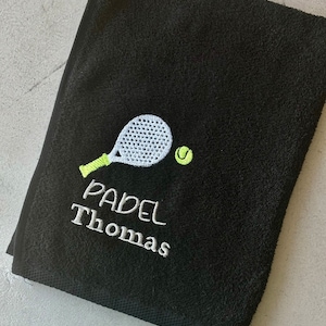 Puede incluir: Toalla negra con bordado blanco de una raqueta de p&aacute;del y una pelota. El texto "PADEL Thomas" est&aacute; bordado debajo de la raqueta.