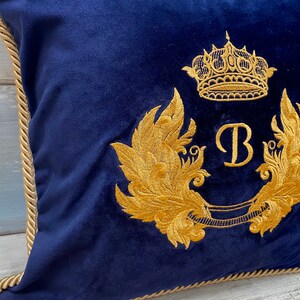 May include: A navy blue velvet pillow with a gold embroidered crown, wings, and the letter "B".