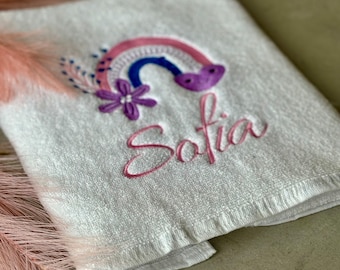 May include: White towel with a pink, blue, and purple embroidered rainbow with a flower and the name "Sofia" embroidered below.
