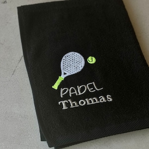 Puede incluir: Toalla negra con una pala bordada en blanco y una pelota de tenis verde. El texto "PADEL Thomas" est&aacute; bordado en blanco debajo de la pala.