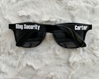 May include: Black sunglasses with the text "Ring Security" on one side and "Carter" on the other side.