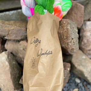 Könnte beinhalten: Eine braune Papiertüte gefüllt mit bunten Garnknäueln. Die Tüte trägt den Text "Wolle Wunderlust" und einen Stempel mit der Aufschrift "Mit Liebe Handgemacht".