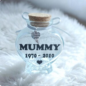 May include: A clear glass heart-shaped jar with a cork stopper and a silver charm that says "I love you." The jar has the word "MUMMY" and the years "1970 - 2010" printed on it, with a black heart below.