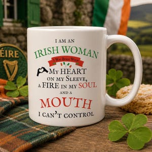 May include: A white ceramic mug featuring the text I AM AN IRISH WOMAN I WAS BORN WITH MY HEART ON MY SLEEVE, A FIRE IN MY SOUL AND A MOUTH I CAN'T CONTROL, accented with green and red lettering, a small Irish flag graphic, and a hand heart icon.