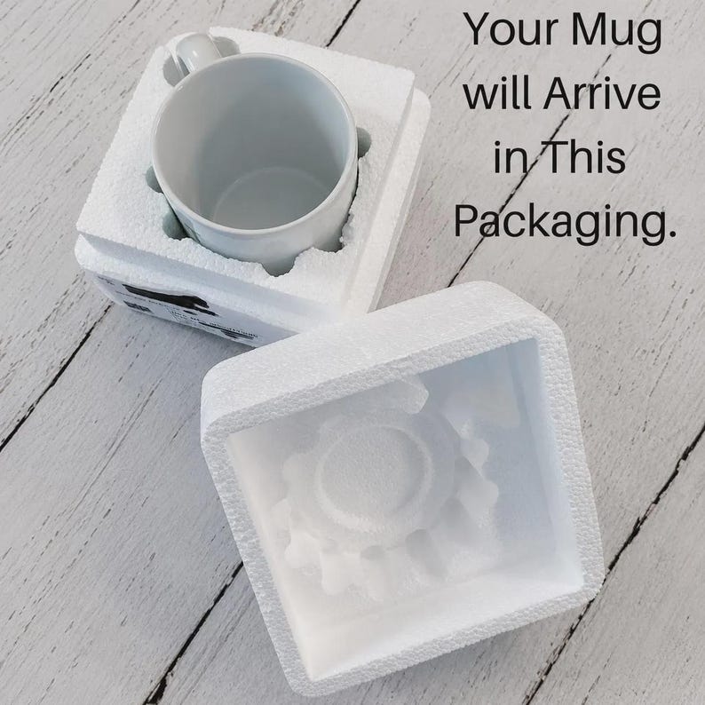 May include: A white ceramic mug nestled inside a custom-fitted white styrofoam protective box, with a separate matching styrofoam lid placed nearby. The text "Your Mug will Arrive in This Packaging." is printed in black on the right side.