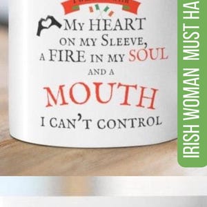 May include: A white ceramic mug featuring the text I AM AN IRISH WOMAN I WAS BORN WITH MY HEART ON MY SLEEVE, A FIRE IN MY SOUL AND A MOUTH I CAN'T CONTROL. The design includes a red banner with green and orange accents and a black heart icon.