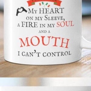 May include: A white ceramic mug featuring the text I AM AN IRISH WOMAN I WAS BORN WITH MY HEART ON MY SLEEVE, A FIRE IN MY SOUL AND A MOUTH I CAN'T CONTROL. The design includes a red banner with the Irish flag and a black heart hand gesture.
