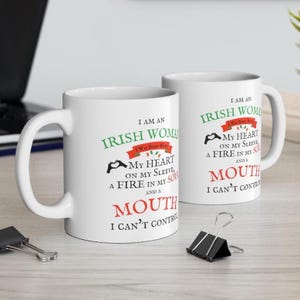 May include: Two white ceramic mugs featuring black, green, and red text that reads: I AM AN IRISH WOMAN I WAS BORN WITH MY HEART ON MY SLEEVE, A FIRE IN MY SOUL AND A MOUTH I CAN'T CONTROL. The design includes a small heart-shaped hand icon.