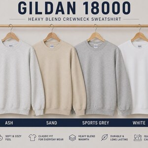 K&ouml;nnte beinhalten: Vier Gildan 18000 Heavy Blend Rundhals-Sweatshirts h&auml;ngen an einer Holzstange. Die Farben von links nach rechts sind Ash, Sand, Sports Grey und White. Jedes Sweatshirt hat lange &Auml;rmel, einen gerippten Rundhalsausschnitt und gerippte B&uuml;ndchen.