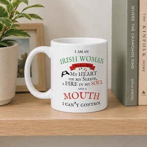 May include: A white ceramic mug featuring black, green, and red text that reads: I AM AN IRISH WOMAN I WAS BORN WITH MY HEART ON MY SLEEVE, A FIRE IN MY SOUL AND A MOUTH I CAN'T CONTROL, accompanied by a small heart-hand icon and two tiny flags.