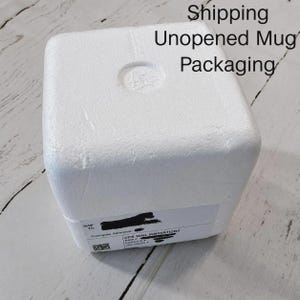 May include: A white square styrofoam shipping container for a mug. The top surface has a circular indentation in the center. A white shipping label is attached to the side with the text Shipping Unopened Mug Packaging visible above.