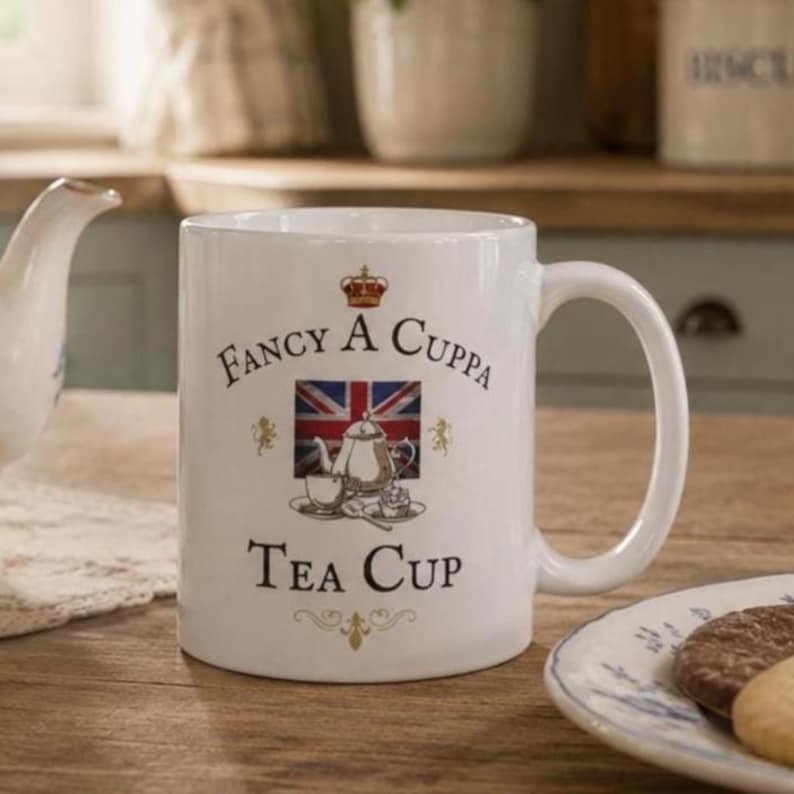 BRITISH TEA Gift Idea Teacup Funny Mug United Kingdom Gag Gift Great Britain Uk Expat Citizen Present Fancy A CUPPA Coffee Cup Union Jack Includes: A white ceramic mug featuring the text "Fancy A Cuppa Tea Cup" in black lettering. The design includes a central illustration of a teapot and teacup set against a Union Jack flag, topped with a small red crown and gold lion accents.