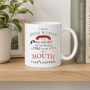 May include: A white ceramic mug featuring black, green, and red text that reads: I AM AN IRISH WOMAN I WAS BORN WITH MY HEART ON MY SLEEVE, A FIRE IN MY SOUL AND A MOUTH I CAN'T CONTROL, accompanied by a small heart-shaped hand icon and flag.