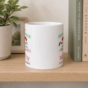 May include: A white ceramic mug featuring printed text in green, red, and black. The text reads: I am an Irish woman, I wear my heart on my sleeve, a fire in my soul, and a mouth I can't control. The design includes a small red ribbon and black heart icon.