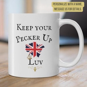 May include: A white ceramic mug featuring the black text Keep Your Pecker Up Luv, a graphic of the Union Jack flag, and a small gold crown icon. The design includes decorative flourishes below the text and a handle on the right side.