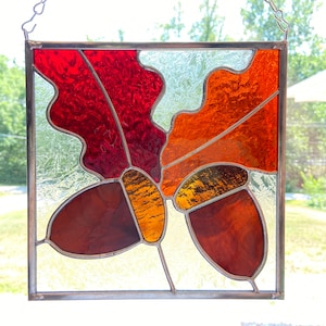 May include: A stained glass window featuring two acorns with oak leaves in shades of red, orange, and brown.