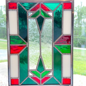 K&ouml;nnte beinhalten: Ein Buntglasfenster mit einem geometrischen Muster aus roten, gr&uuml;nen und wei&szlig;en Glasscheiben. Das Fenster ist in silberfarbenem Metall gefasst und h&auml;ngt an einer Kette.