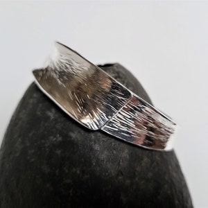 May include: A silver bracelet with a textured, hammered finish. The bracelet is wide and has a curved shape.